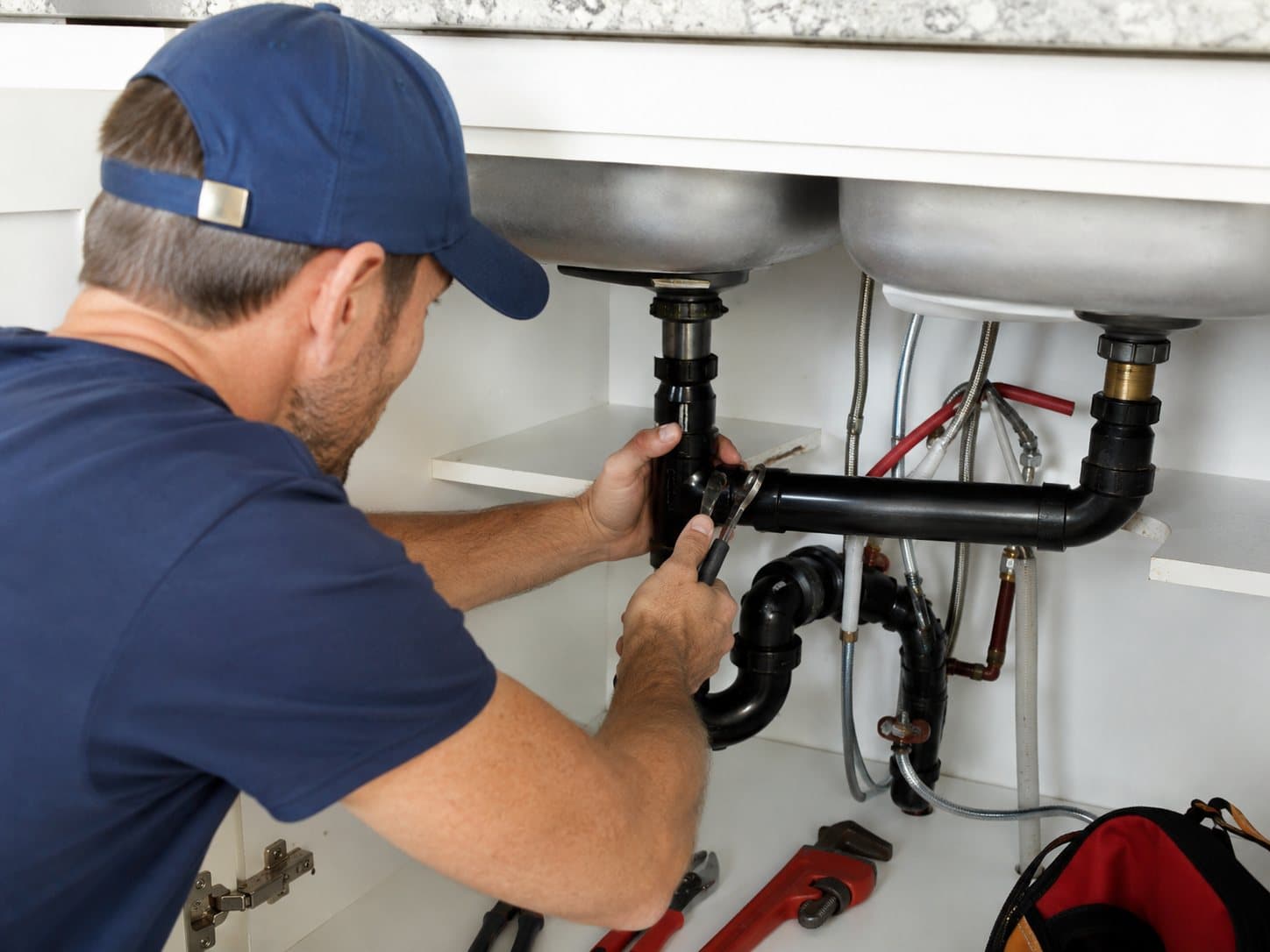 A Maple Ridge plumber tightening a P-trap fitting under a kitchen sink